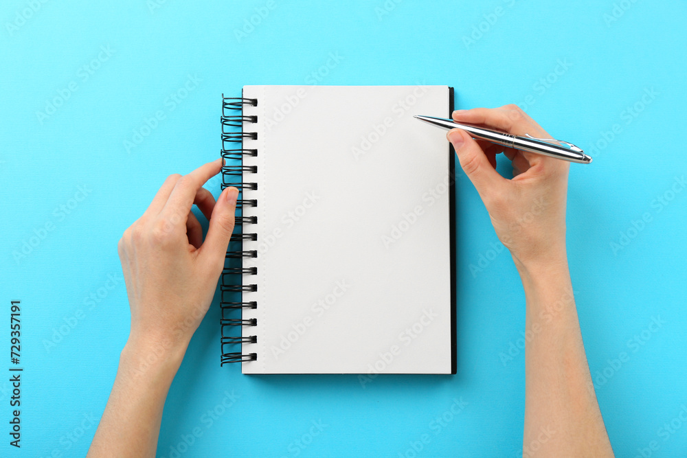 Woman writing in notebook on light blue background, top view Woman writing in notebook on light blue background, top view