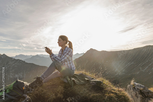 Woman hiking and enjoying the evening sun while on her cell phone at the top of a mountain. Achenkirch, Tirol, Austria photo