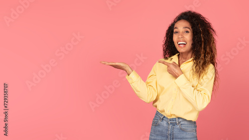 Happy black woman presenting something with hand on coral background