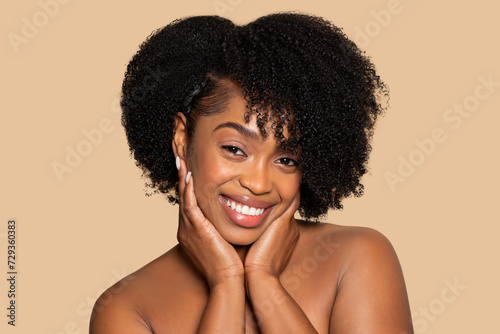 Joyful african american woman with hands on cheeks and curly hair  beige backdrop