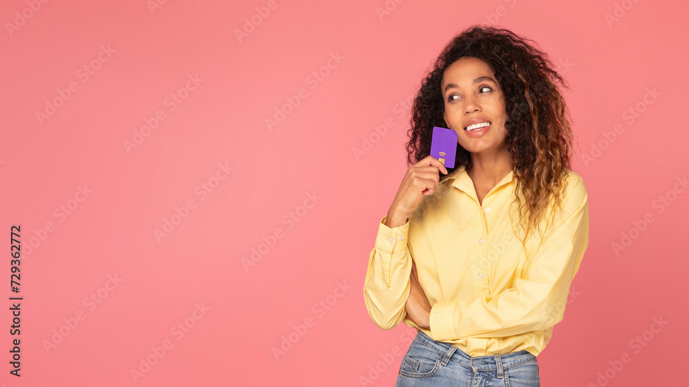 Thoughtful woman shopper with credit card on coral pink background Thoughtful woman shopper with credit card on coral pink background