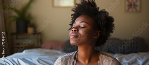 Beautiful African American woman with closed eyes sitting peacefully on the bed.