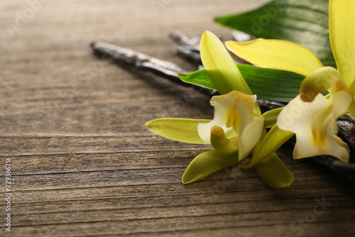 Vanilla pods  beautiful flowers and green leaves on wooden table  closeup. Space for text