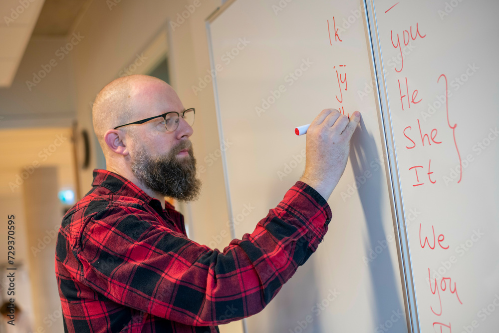 Teacher in class writing on white board with a marker Teacher in class writing on white board with a marker