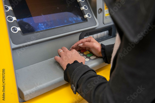 young woman taking money out of her atm, cashmachine covering her pin for security photo