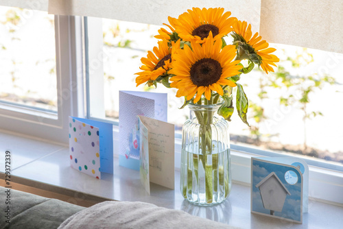 Close up of sun flowers in a vase over the window with birthday cards  photo