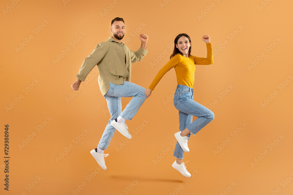 couple jumping shaking their clenched fists in celebration, orange background