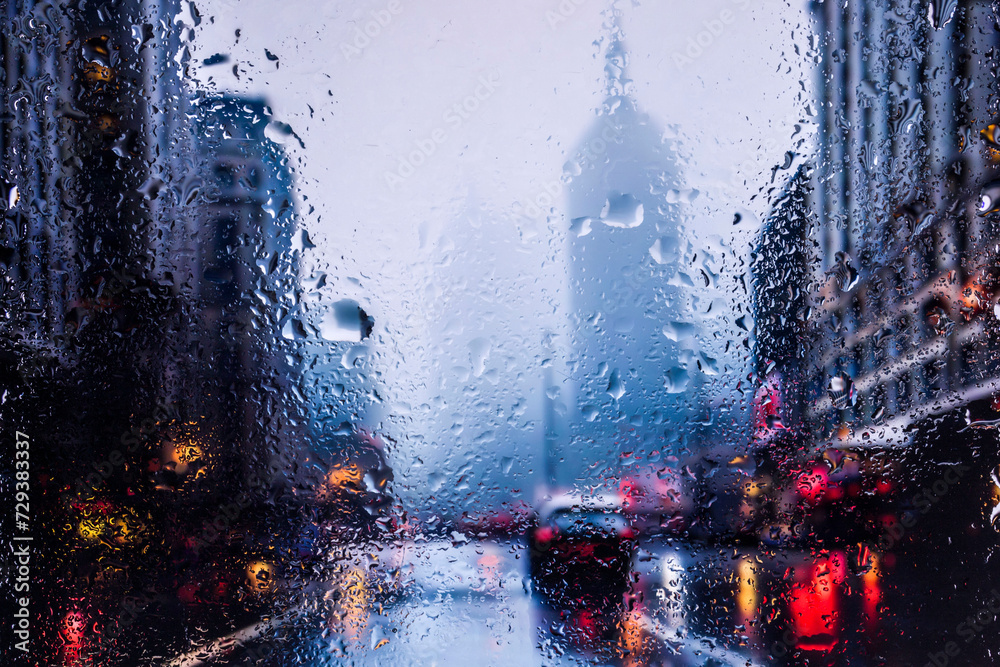 View through a glass window with raindrops on city streets with cars in ...