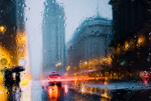 Fototapeta Naklejka Na Ścianę i Meble -  View through a glass window with raindrops on a blurred silhouette of a girl on a autumn city street after rain against the bokeh of city lights, night street scene. Focus on raindrops on glass	