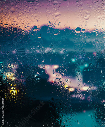 View through a glass window with raindrops on city streets with cars in the rain, bokeh of colorful city lights, night street scene. Focus on raindrops on glass 