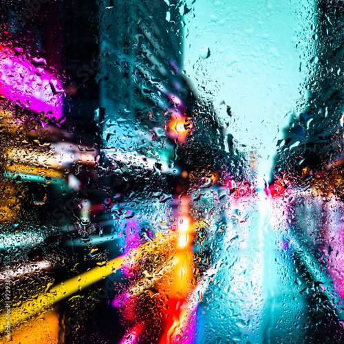 Fototapeta Naklejka Na Ścianę i Meble -  View through a glass window with raindrops on city streets with cars in the rain, bokeh of colorful city lights, night street scene. Focus on raindrops on glass