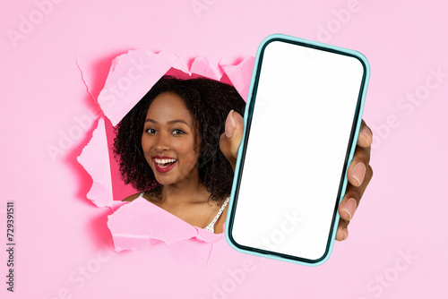 black lady holding cellphone showing through hole in pink background © Prostock-studio