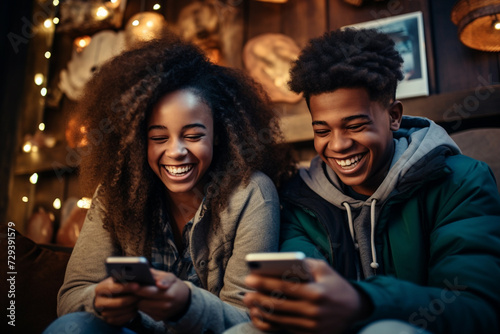 Two African American teenagers students sit together laughing looking in phone screens of their mobile phones. Problem of free time spending of young people concept