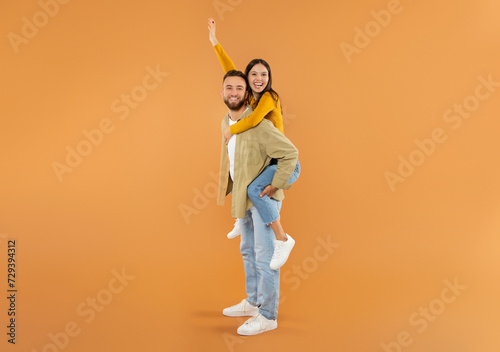Cheerful young man giving piggyback ride to his wife, studio