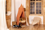 Rustic playroom interior with rattan crib with canopy, wicker baskets, toys and window. Wickered cradle bed with baldachin in newborn room in scandi style at home. Black racing car toy in a child room