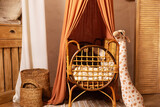 Rustic playroom interior with rattan crib with canopy. Stylish scandi interior of newborn baby room with baby cot bed. Hanging canopy with cradle in nursery room. Decor children room with furniture. 