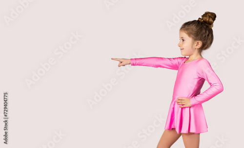 Portrait of a little gymnast girl in pink dress pointing with index finger to one side picture for advertising banners or promotions.