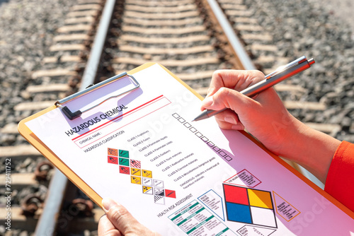 Action of an engineer is checking on chemical hazardous material checklist form with background of train freight tanker for crude oil or chemical cargo. Industrial safety working scene. 