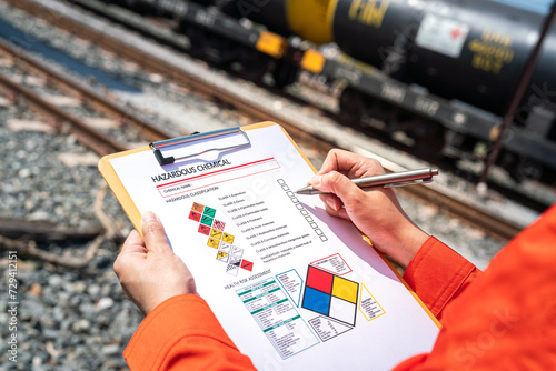 Action of an engineer is checking on chemical hazardous material checklist form with background of train freight tanker for crude oil or chemical cargo. Industrial safety working scene.  photo