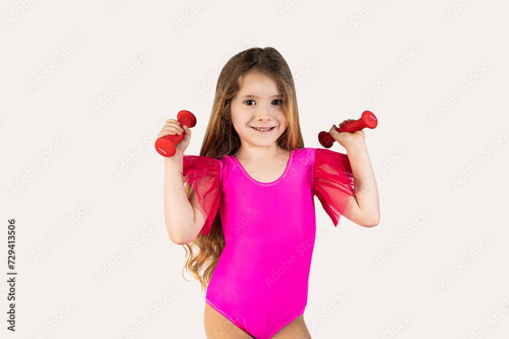 Close-up portrait, child, smiling, funny looking, happy little girl wearing pink gymnastics leotard, lifting dumbbells, isolated white background. Facial expressions, emotions, attitude, determination