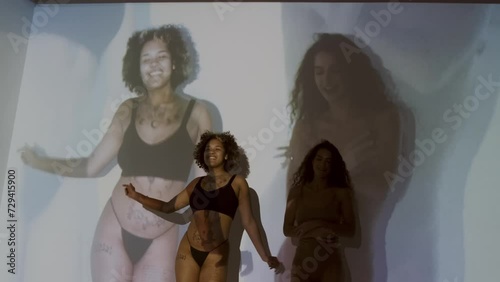 Horizontal medium long studio shot of young Black and Caucasian women in underwear dancing together with their image projected on backgroundHorizontal medium long studio shot of young Black and Caucas photo