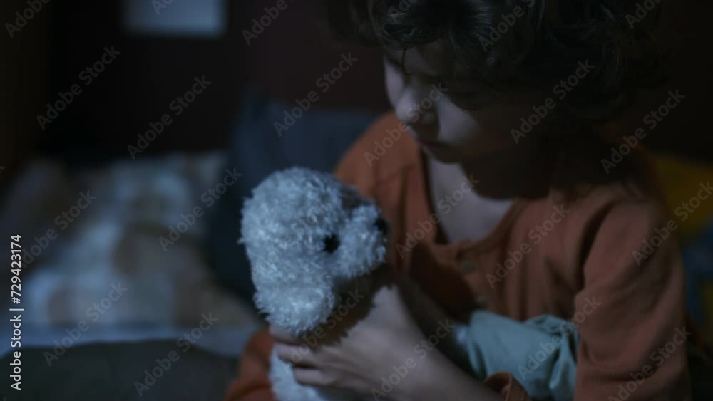 Side closeup of Caucasian curly boy sadly looking at window and hugging white stuffed puppy at night while dreaming of pet dog Side closeup of Caucasian curly boy sadly looking at window and hugging white stuffed puppy at night while dreaming of pet dog