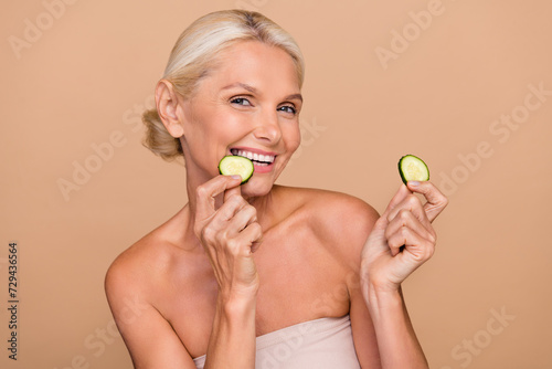 Photo portrait of pretty retired female daily morning beauty routine skin hold cucumbers shoulders off isolated on beige color background