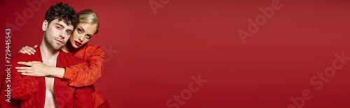 beautiful young woman with red lips and blonde hair embracing handsome man in red attire, banner