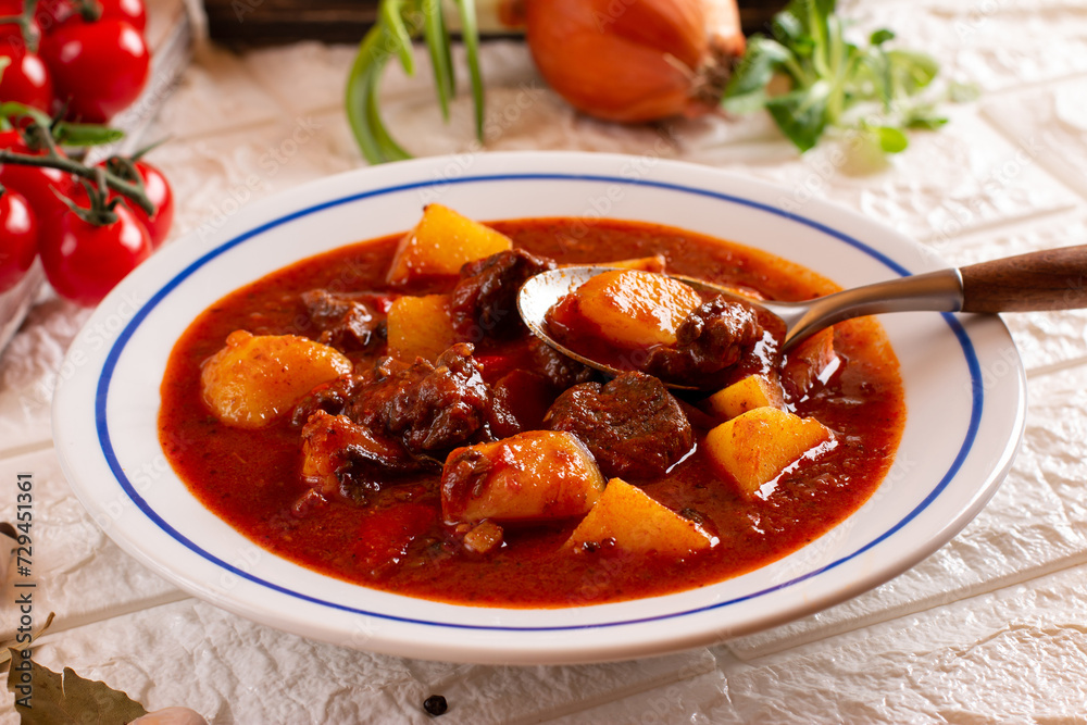 Pork goulash meat and potatoes on plate, garlic, onion, tablecloth in the background - typical Czech food Pork goulash meat and potatoes on plate, garlic, onion, tablecloth in the background - typical Czech food