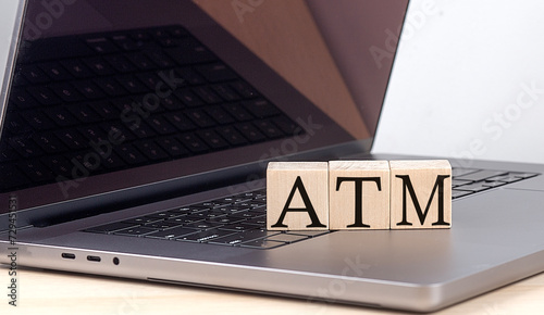ATM word on wooden block on laptop, business concept