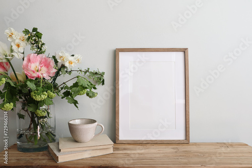 Easter breakfast still life. Blank picture frame mockup. Wooden bench, table composition with cup of coffee, old books. Spring bouquet of pink tulips, white daffodils. Hawthorn, guelder rose flowers. © tabitazn