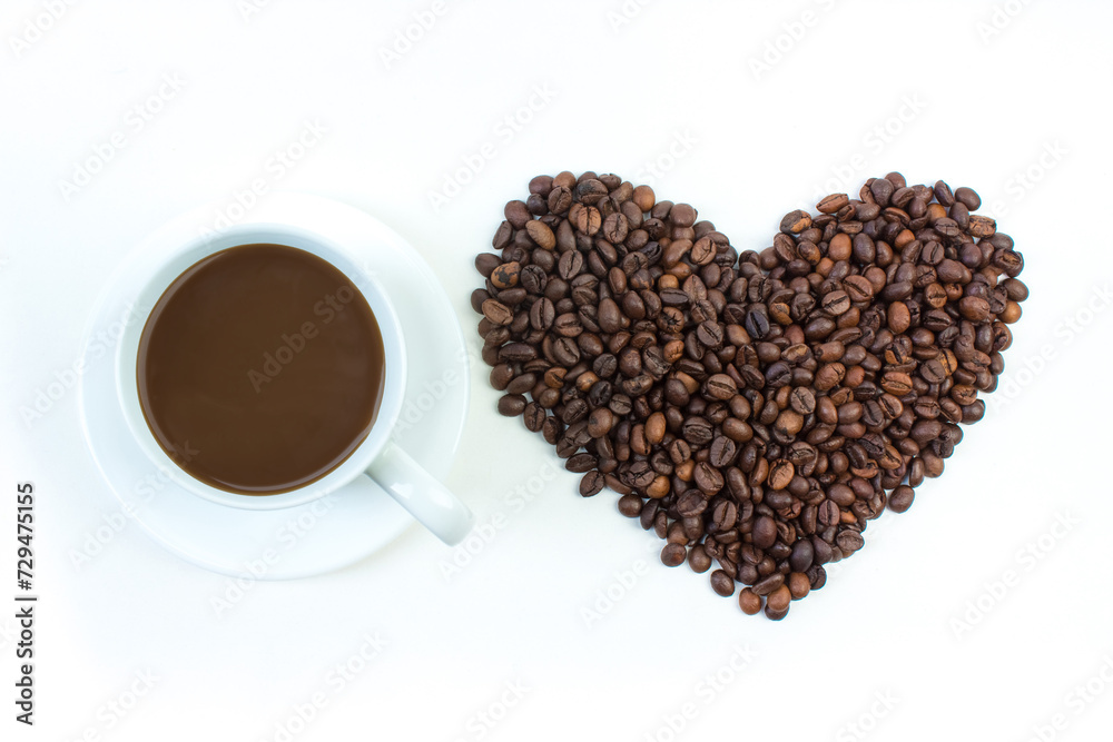 A pile of coffee beans in the shape of a heart, a cup of coffee on a white background. Top view. A pile of coffee beans in the shape of a heart, a cup of coffee on a white background. Top view.