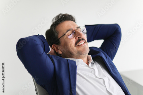 Obraz na plátně Relaxed businessman in a blue suit reclining in his chair with his hands behind