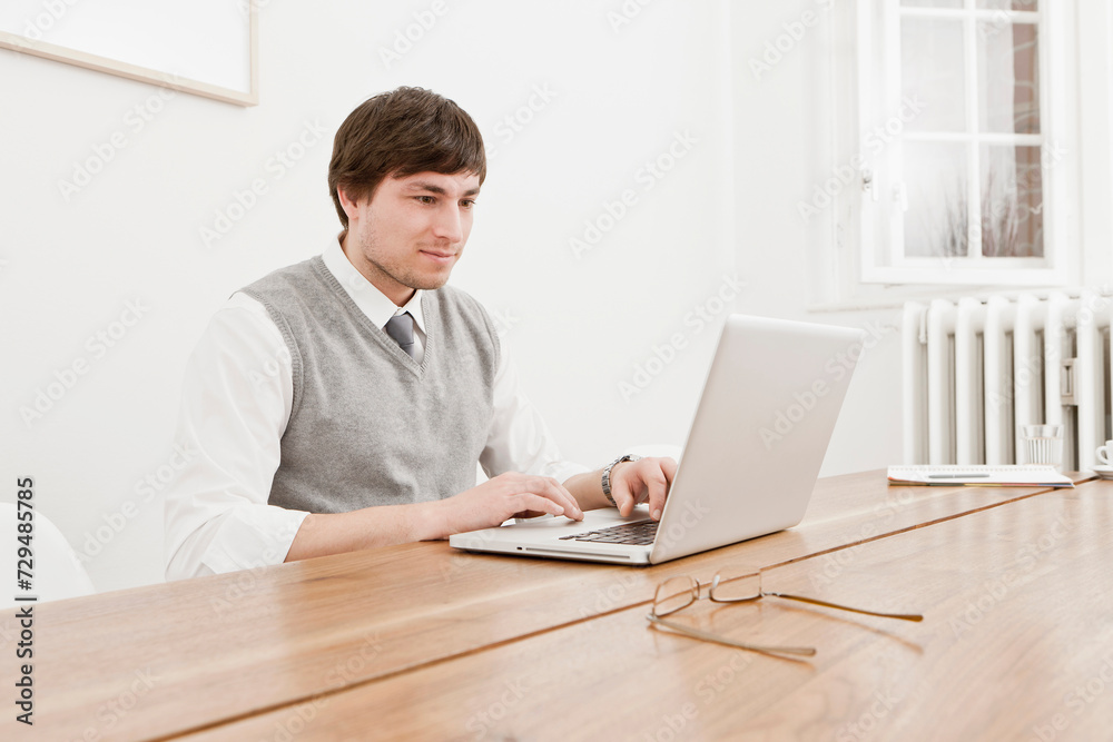 Young professional in business attire in an office of a small start up company with cell phone and, computer and documents. Munich, Germany Young professional in business attire in an office of a small start up company with cell phone and, computer and documents. Munich, Germany