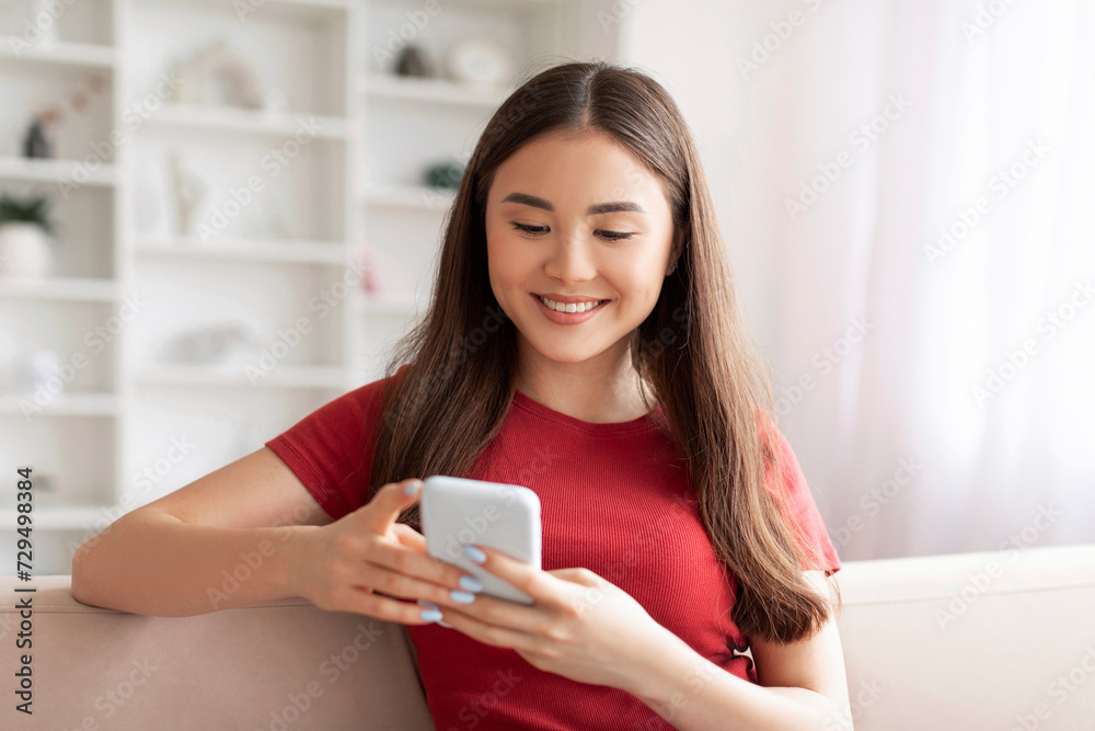 Smiling young asian woman focused on texting with her smartphone at home Smiling young asian woman focused on texting with her smartphone at home