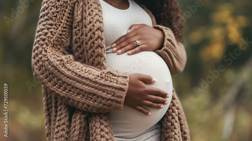 Close up of pregnant woman in knitted sweater touching her belly in autumn park. AI. photo