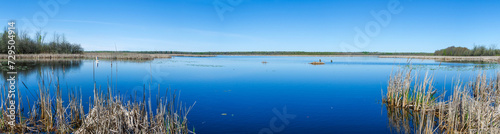 Panorama of a conservation area pond with blue sky and still water