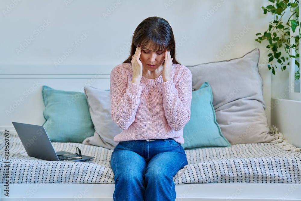 Unhappy mature woman experiencing headaches stress depression sitting on couch at home Unhappy mature woman experiencing headaches stress depression sitting on couch at home