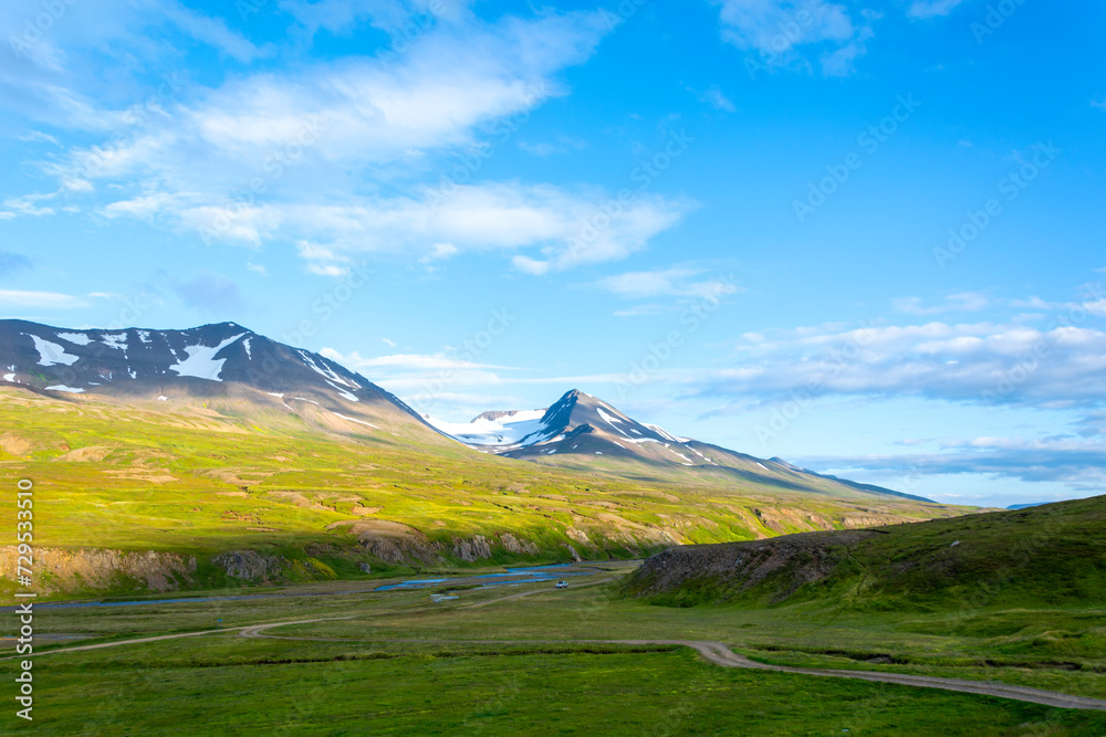 Icelandic summer landscape with green meadow, mountains and blue sky