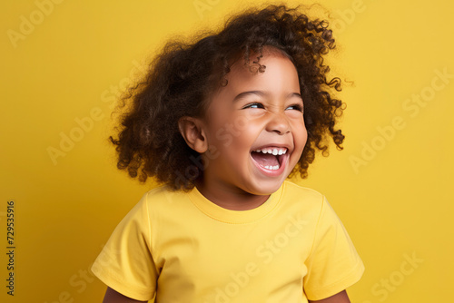 Laughing happy african american kids child todler wearing a yellow t-shirt on yellow background. Dark-skinned child smiles, rejoices, portrait. Preschool education concept, kindergarten
