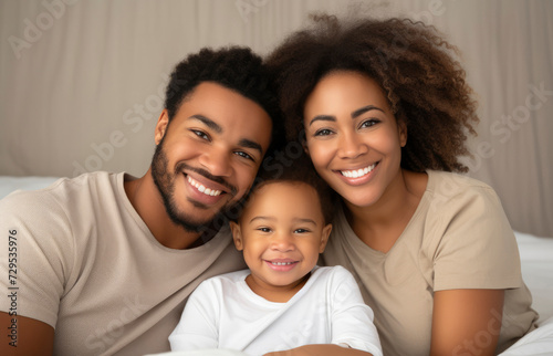Young beautiful African American family, mom, dad and little child smiling and looking at the camera on a light background. Happy parents, motherhood, family, love, mother's day © FoxTok