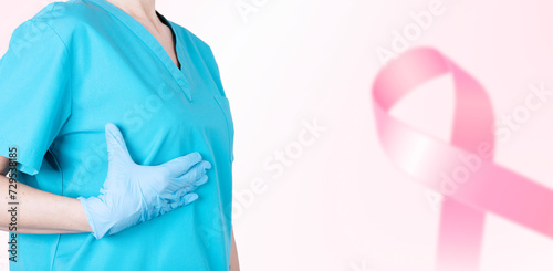 A female doctor in a medical uniform supports her breasts and a pink ribbon as a symbol of breast cancer awareness. Medical pink background. Poster. copy space.