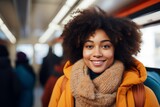 An engaging young woman with a full curly afro wears a snug scarf and a bright smile, adding warmth to the city train atmosphere