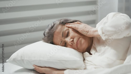 An elderly woman wakes up with a severe headache, a result of poor sleep photo