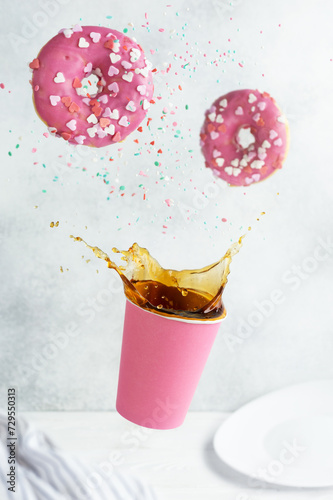 Paper cup with splashes of coffee drink or tea and donut on a gray background. Creative fashionable levitation. Valentine's day.