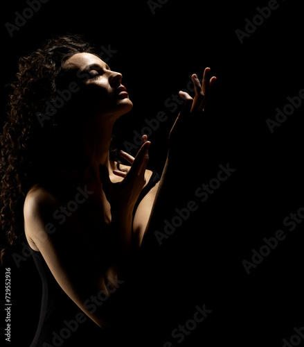 Sensual portrait silhouette of beautiful curly woman with outstretched hand sings in backlight on a black background