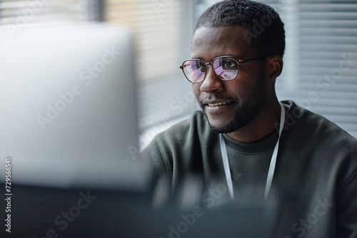 Closeup portrait of professional Black young man wearing glasses with computer screen reflection in office copy space