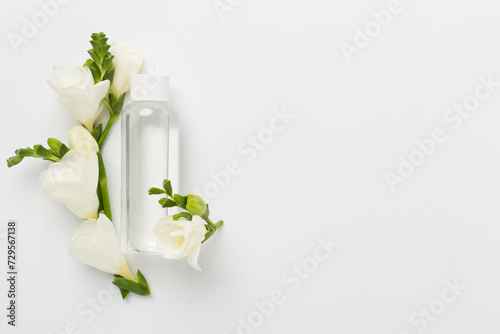 Cosmetic bottle with freesia flowers on color background, top view photo