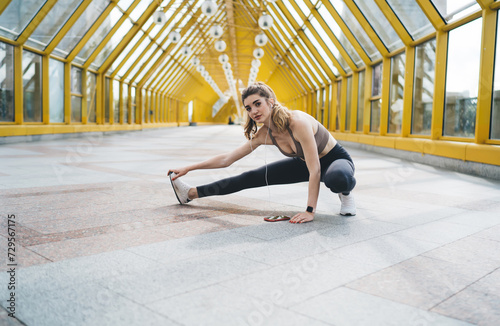 Committed young Caucasian woman performing a side stretch in a luminous, yellow architectural overpass, demonstrating flexibility and focus during her urban fitness routine