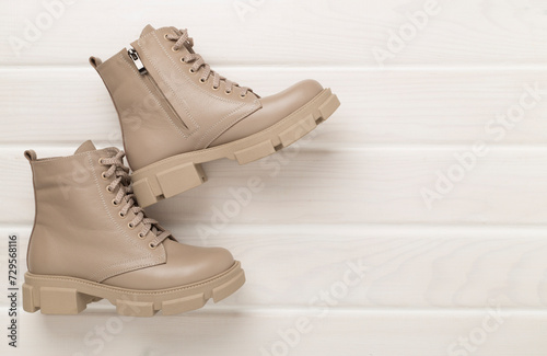 Beige trendy boots on wooden background, top view.